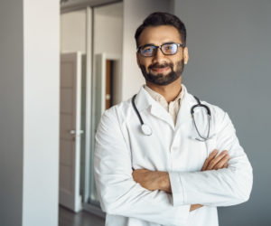Portrait of male doctor in white coat and stethoscope standing in clinic hall
